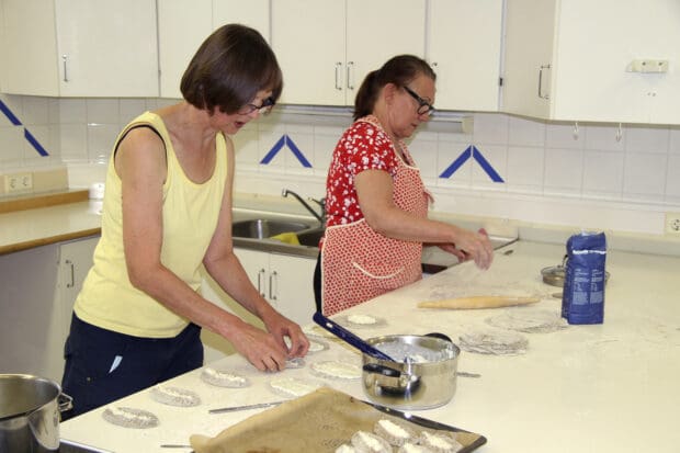 Juupajoen Karjala-Seuran puheenjohtaja Taru Iivonen (vas.) kertoo, että piirakoita oli tarkoitus valmistaa talkoissa reilu 300 kappaletta torikahviota varten. Hannele Kylmälä kauli taikinaa pulikalla. Kuva: Markus Puolakanaho